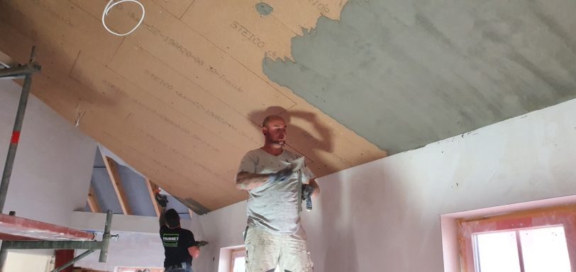 Mineralische Putzarbeiten im Innenbereich Arbeiter mit Pinsel und Farbe, der eine Decke in einem Raum streicht.